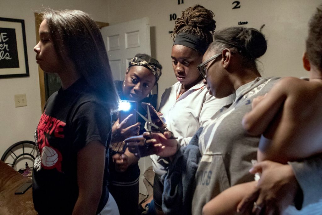 First Place, Ron Kuntz Sports Photographer of the Year - Jessica Phelps / Newark AdvocateTashia Croom trims the last little long strands from her daughter, Taliyah's hair while her younger sisters, Taya and Tavia hold up lights and help her. The 3 sisters are extremely close. Most evening one or both of them drop by Tashia's home. They all coach volleyball for middle school and high school, along with their mom, Shela. The sisters also coach middle school basketball. Taliyah plays both sports at the high school. 