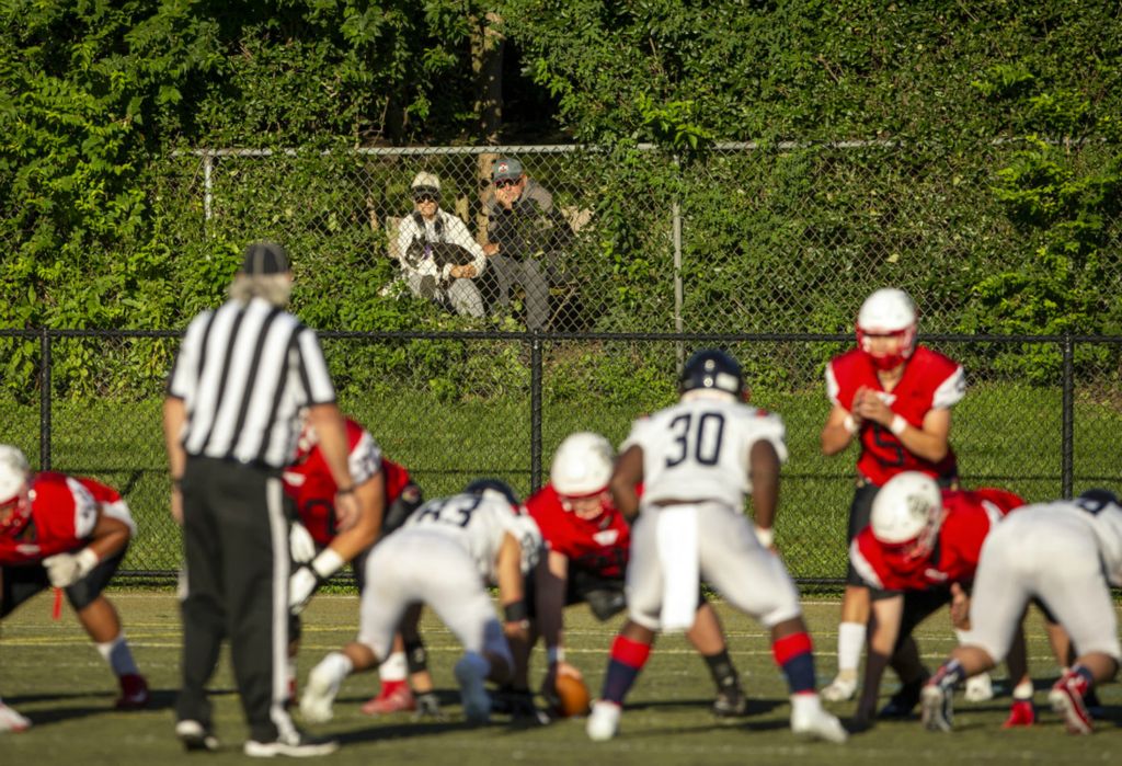 First Place, Team Picture Story - Adam Cairns / The Columbus Dispatch, “Social Distancing”Barb and Rick Weber, with their dog Sadie, take advantage of a hole in the greenery behind their condo to watch the high school football game between St. Charles Prep Cardinals and the Bishop Hartley Hawks at St. Charles Preparatory School in Columbus on Friday, Sept. 18, 2020.