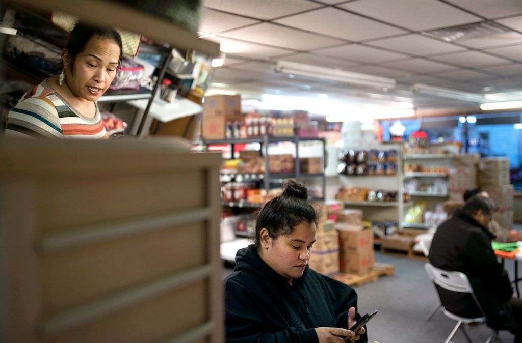 First place, Chuck Scott Student Photographer of the Year - Erin Burk / Ohio UniversityLydia Bolkheim, left, and Primrose Joash, center, discuss shipments for the Ralik Ratak Alele store, one of two Marshallese groceries in Celina, Ohio, on November 13, 2021. Lydia often helps people translate their online Medicare applications out of the store, which she runs with her fiance, Robinson Lee. Robinson has been planning to apply for grant funding to provide more Medicare application assistance, but the Marshallese Coalition has recently been disbanded following the approval of Medicaid for the community. "I am just waiting for something that can help," he says. Lydia's mother's side of the family were living on Rongelap Atoll at the time of the largest nuclear detonation tested on Bikini Atoll, called "Castle Bravo."  Regarded as the worst radiological disaster in U.S. history, this explosion carried nuclear fallout along the wind currents to Rongelap. Lydia, along with many of her family members, has dealt with cancer which she attributes to the tests. Because of restrictive Medicare availability, she has had to travel to other states for care in the past.
