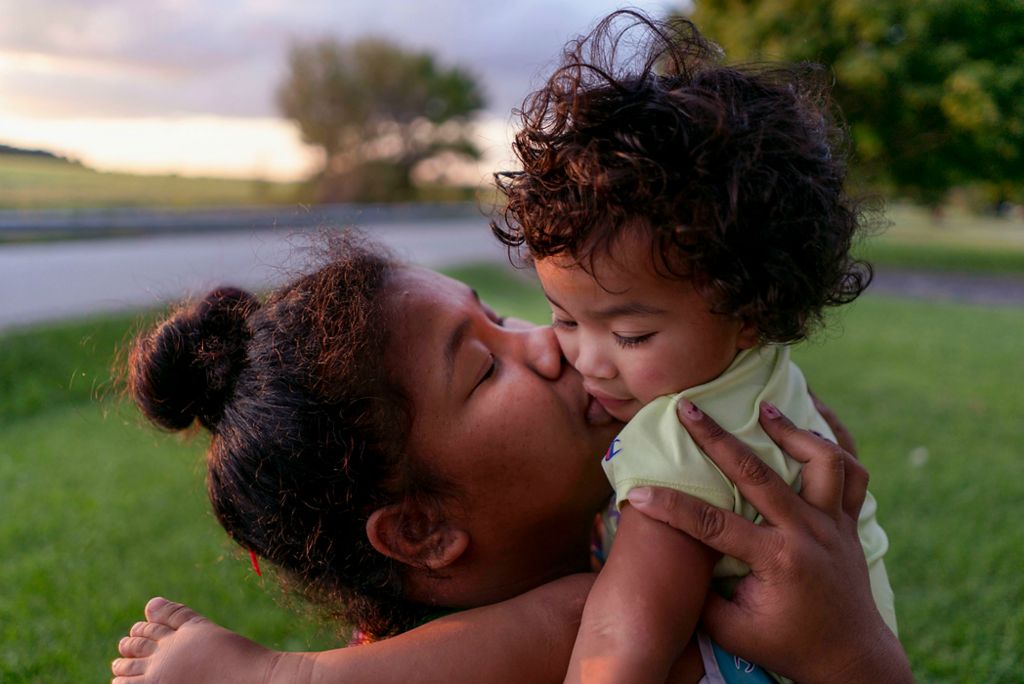 First place, Feature Picture Story - Erin Burk / Ohio University, "Medicare"Jacintha Betti kisses her daughter, Aidrielyann in their yard in Union City, Ohio, on September 9, 2021. Jacintha moved to the United States from the Republic of the Marshall Islands after falling in love with her boyfriend, Michael, while he and his dad visited the islands. Most people migrate to the U.S. from the Republic of the Marshall Islands for job opportunities. 