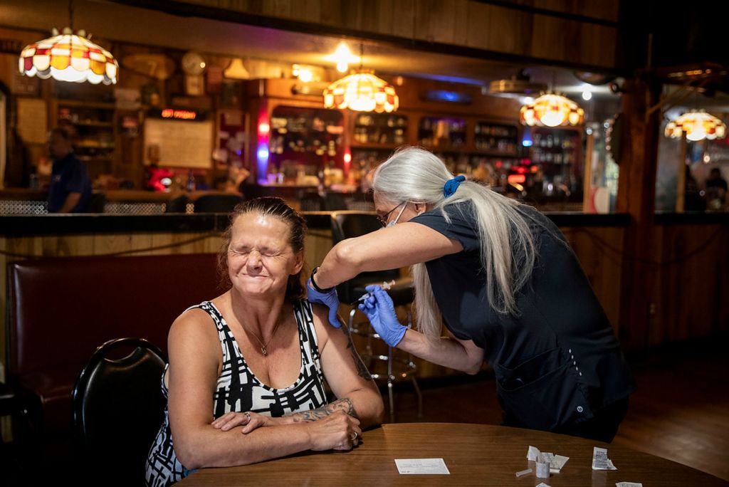 Third place, Feature Picture Story - Meg Vogel / The Cincinnati Enquirer, "Vaccine Hesitancy"Kim Neace, a nurse practitioner, administers the Johnson & Johnson COVID-19 vaccine to Lisa Walker at the Long Branch Tavern in Laurel, Indiana, on June 7, 2021. After Walker's 15 minute observation period, she took a shot of tequila as part of the "shot for a shot" promotion by the Franklin County Health Department. Four out of five people in Franklin County are unvaccinated – the lowest vaccination rate in Greater Cincinnati and the fourth-lowest among Indiana's 92 counties. Poor, rural towns like Laurel, where the median income is about half that of the rest of the nation, are a big reason why. Fear, distrust and politics still dominate conversations about the vaccine among Laurel's 500 residents, complicating the job of public health officials, who worry the growing gap in America between communities with high and low vaccination rates will keep the pandemic going for years.