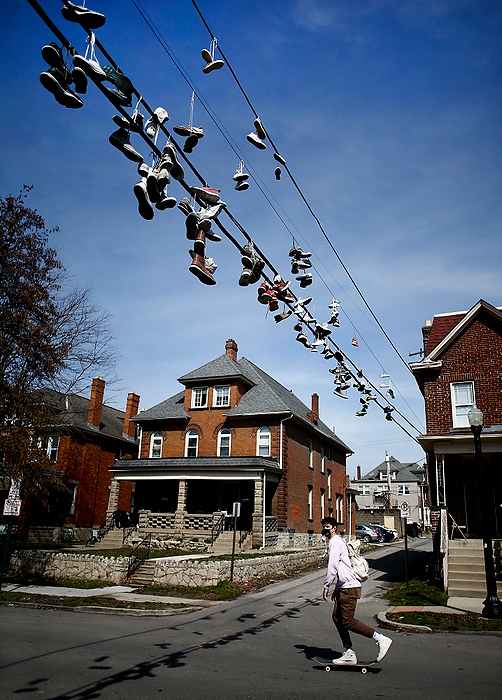 Third place, Pictorial - Fred Squillante / The Columbus Dispatch, "Hanging Shoes"A skateboarder passes under shoes hanging on wires on E. 13th Ave. on March 17, 2021, near The Ohio State University campus. Temperatures in the 60s enticed students living on the street to work on front porches. A student who has lived on the street for two years said the number of shoes hanging on the wires has increased over that time period. She also said maintenance workers and landlords get mad because the shoes bring down wires.