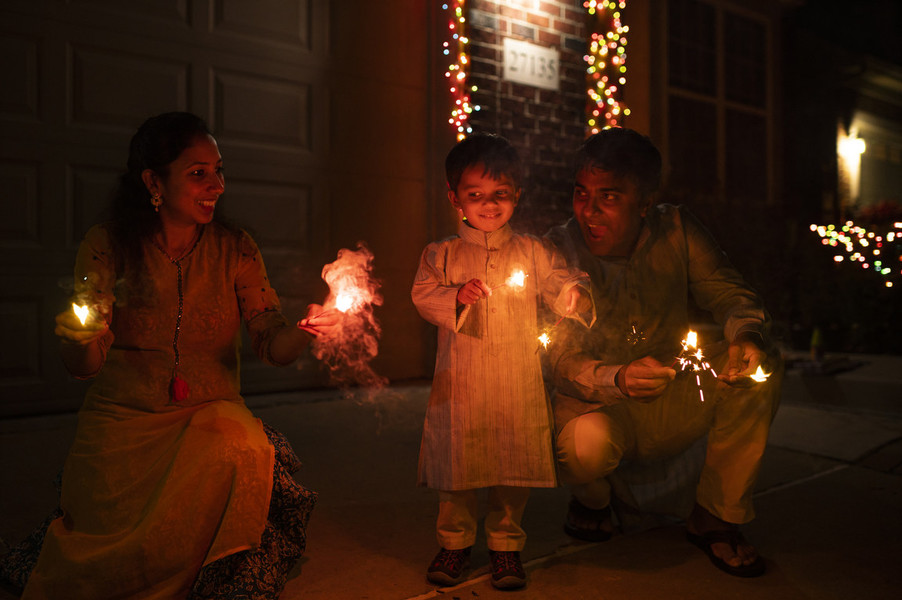 Feature Picture Story - First Place, “Telugu Americans”From left, Keerthi Sanivarapu, 35, Ridhay Vemuri, 2, and Pavan Vemuri, 37, celebrate Diwali (the Hindu festival of lights) by lighting fireworks at their residence in Novi, Michigan. They also adorn their home with lights, a tradition often confused with Christmas lights in the United States.  (Akash Pamarthy / Ohio University)