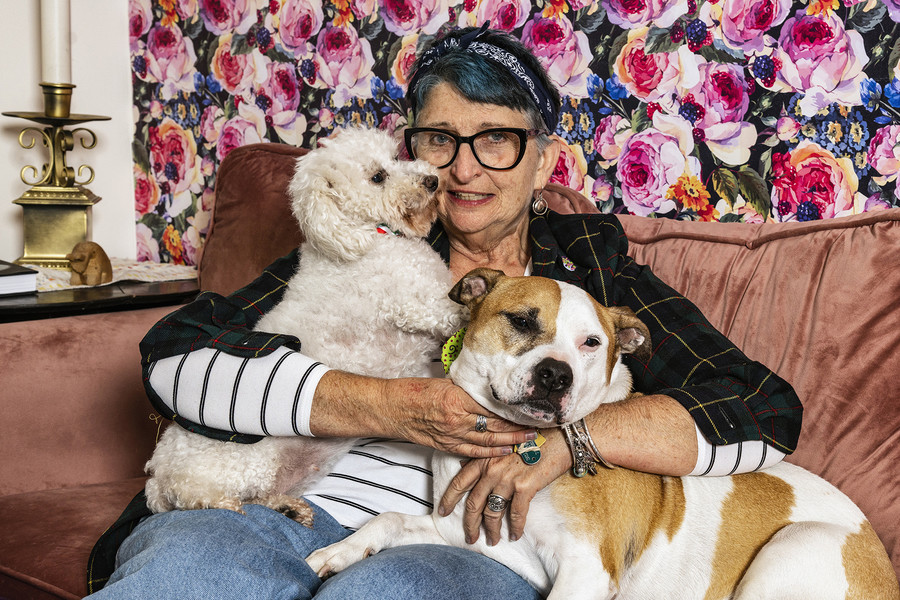 1st - Chuck Scott Student Photographer of the Year Retired early childhood intervention specialist and artist Tina Carnes Kelsey, 67, of Cambridge, poses with her dogs Penny (left) and Sally, at her home in Athens  on Wednesday, November 22, 2023. Kelsey sold her rural home of 25 acres in the incorporated community of Shade and relocated to uptown Athens after ending her relationship with her then-partner John last year. "When we split, I kept the dogs, while he took our three cats," said Kelsey.  (Loriene Perera / Ohio University)