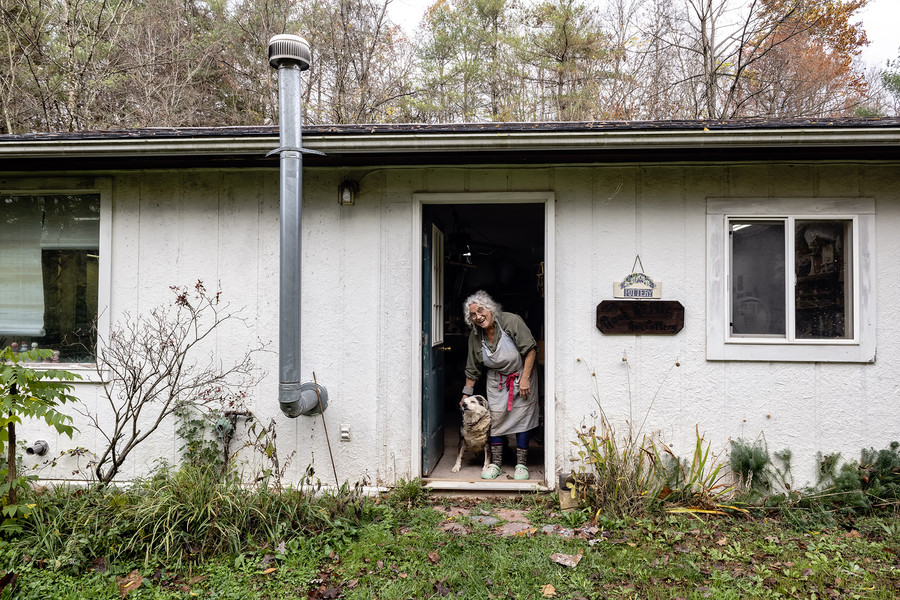 1st - Chuck Scott Student Photographer of the Year Susan "Susie" Rhea Abramovitz, 72, of Youngstown, Ohio, pets her dog Sparky, 17, while posing for a photo by the entrance to her studio Rock Riffle Run Pottery in the unincorporated community of Shade, Ohio, on Tuesday, October 31, 2023. "It’s been 39 years since I moved here from my first studio in Athens. I no longer feel an attachment to my original location. I named my studio after the creek that bordered it and kept it despite my move to Shade as it’s catchy,” Abramovitz shared.   (Loriene Perera / Ohio University)