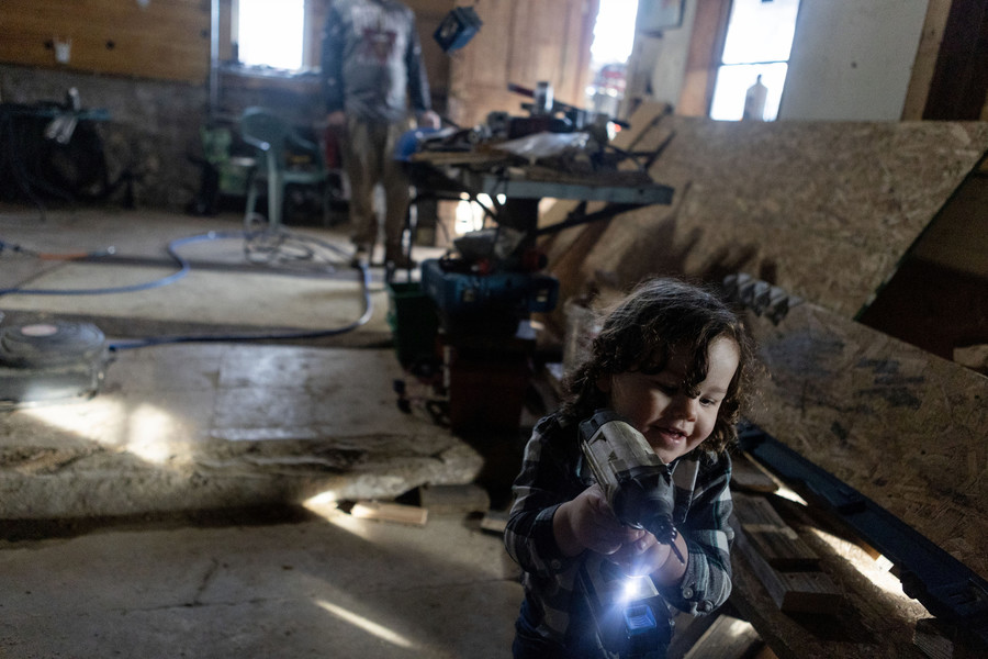 Feature Picture Story - 1st, “Tablertown Psalms ”Lincoln Singer, 2, runs while holding a nail gun into in the tool room of his uncle, as his Father Caleb Singer watches in the background. “Don’t fool around too much with that boy,” Caleb said.  (Michael Blackshire / Ohio University)