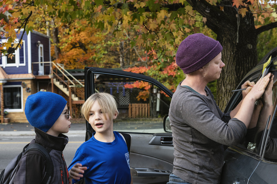 Feature Picture Story - 3rd, “Symphony of Soil”Elias V. Barnes, 9, (center), of Athens, talks to his friend Oliver Martin, 10, of Athens, as his mother, seed farmer Lindsay Klaunig, signs off on a form that informs The Plains Elementary School that Elias will be picked up by Oliver's mother as they wait for the school bus to arrive in Athens, on Wednesday, October 25, 2023. "This is the first year he's going to school in town, in Athens. Before it was the rural school, Alexander. That's our district school. I've never wanted him to go to a rural school. Athens is our community. It's our people. It's our customers. It's most of our friends," Klaunig explained.  (Loriene Perera / Ohio University)