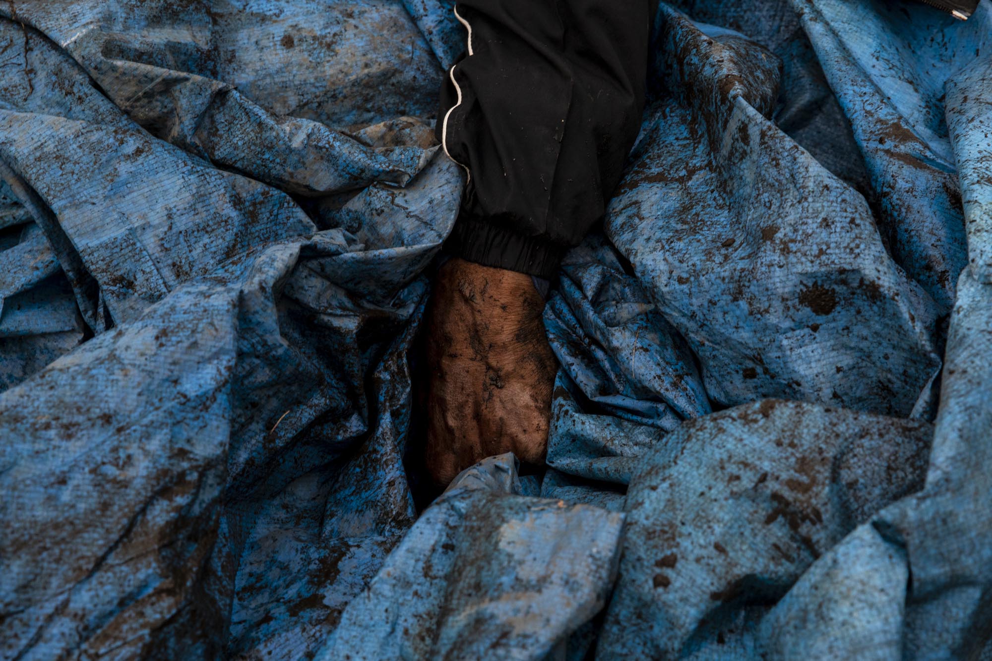 A man carries a tarp he retrieved from the woods behind Tent City. He used the tarp to waterproof the roof of another resident's tent during a heavy rain storm. During especially cold months, residents insulate their tents with donated blankets. However, the humidity created by sleeping in the tent can cause mold to grow, which poses a health risk.